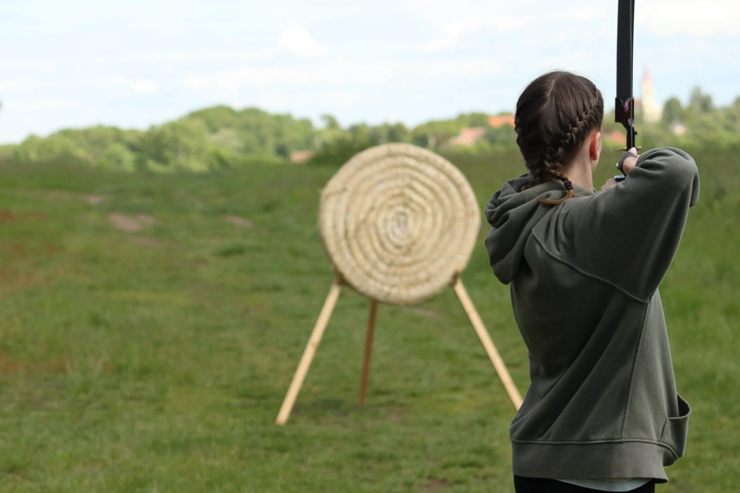 girl shoots from an arrow bow at a straw target in the countryside