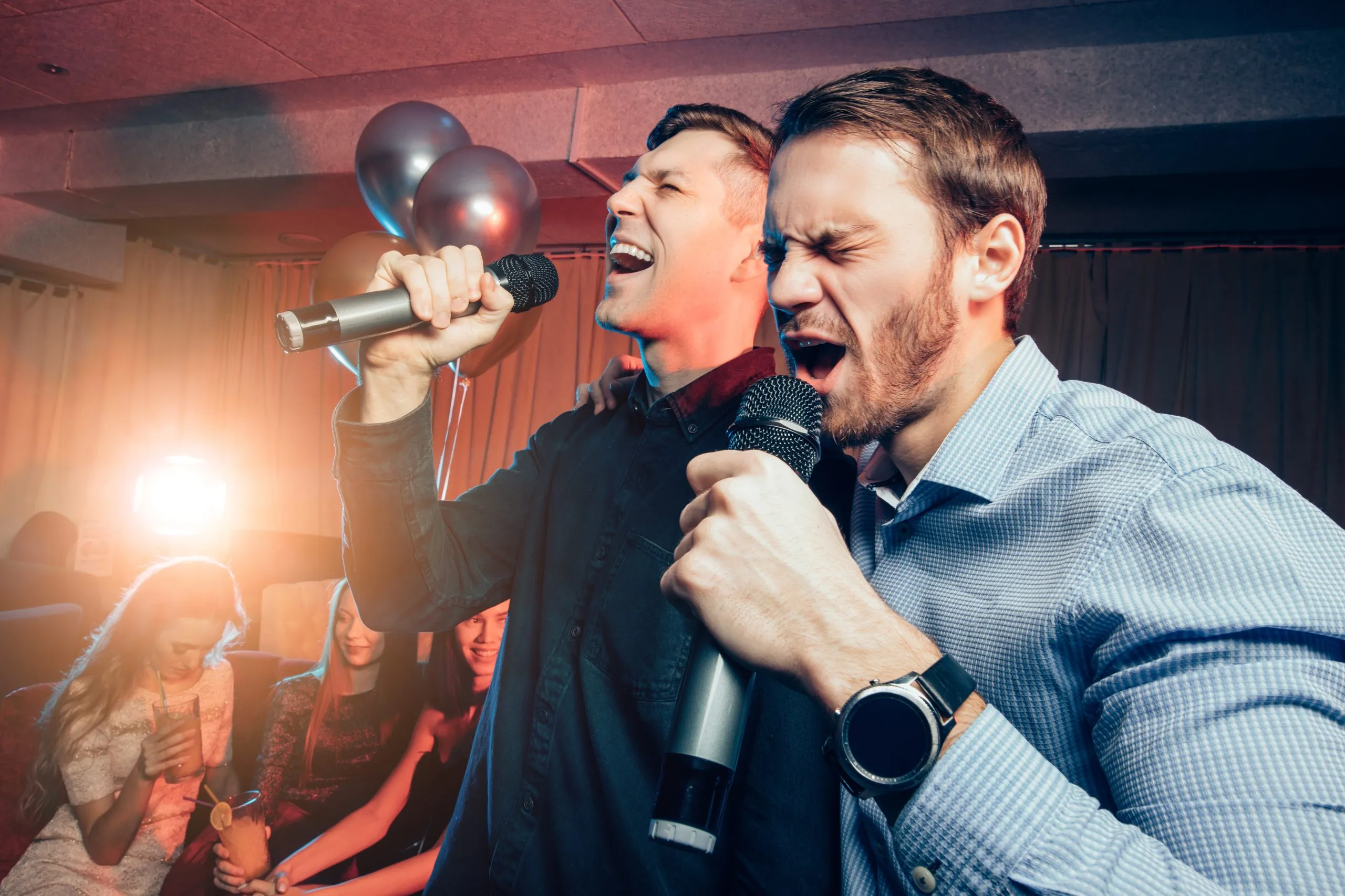 two young caucasian men in t-shirts singing in microphone in karaoke bar, having fun, celebrating. holiday, leisure, party concept