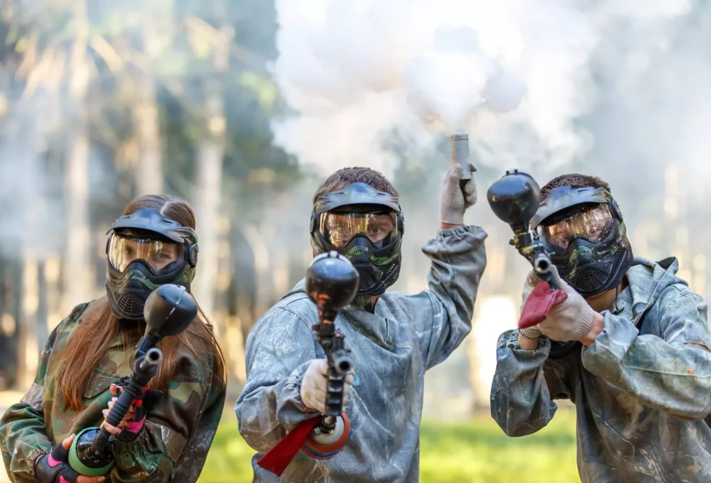 Three paintball players with guns and smoke grenade aiming