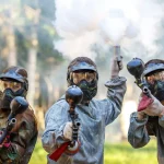 Three paintball players with guns and smoke grenade aiming