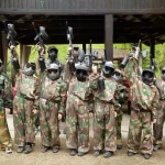 Boys dressed in camouflage stand in a row on a paintball base