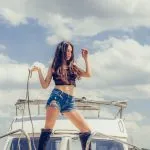 Hot seductive woman in sexy high black boots posing on boat